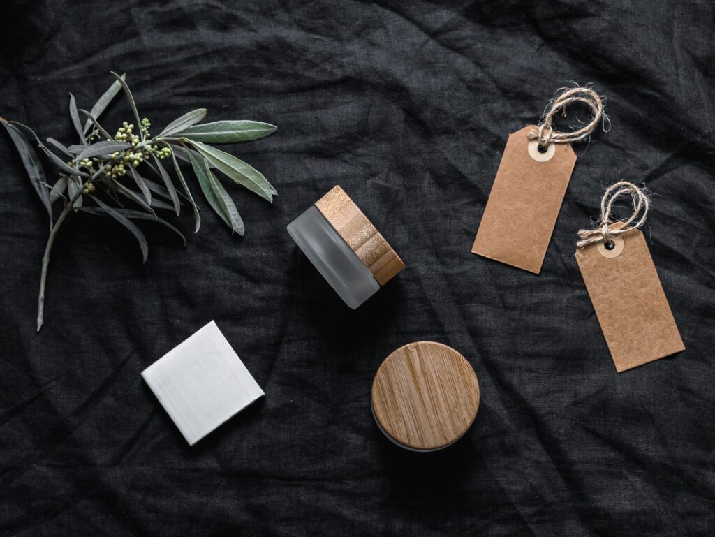 Elegant flat lay of glass jars and paper tags on a black background, accentuated by green leaves for a natural touch.